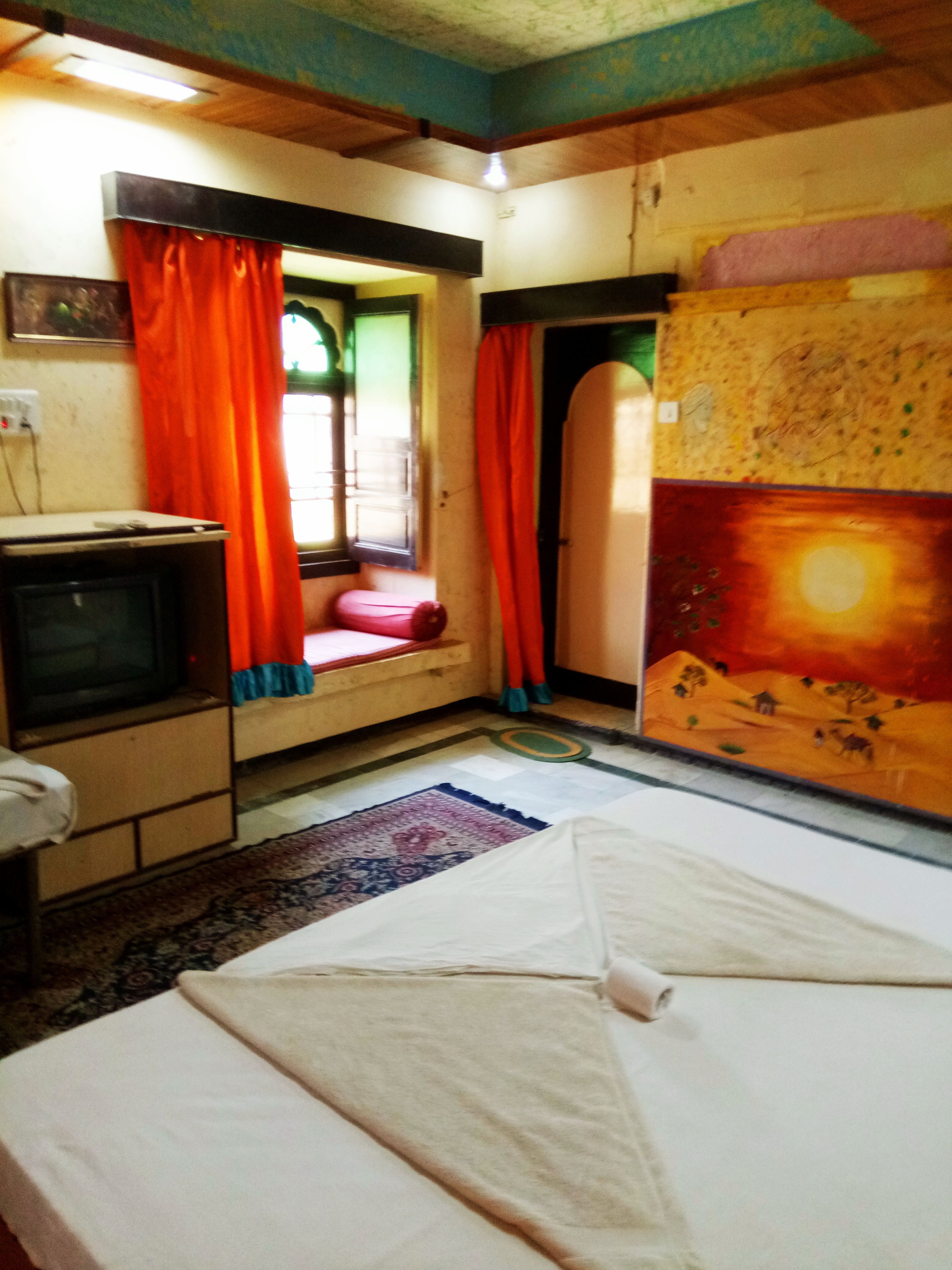 A room with a bed, a television, and a window with curtains.