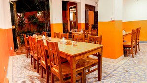 A restaurant with wooden tables and chairs, a tiled floor, and orange walls. - Kathmandu Regency Hotel (Kathmandu)