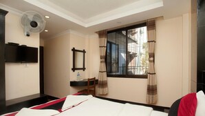 A hotel room with a bed, a desk with a chair, a flat-screen TV, a window with curtains, and a ceiling fan. - Kathmandu Regency Hotel (Kathmandu)