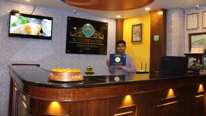 A reception desk with a television displaying a bear, a framed sign for the Kathmandu Regency Hotel, and a man holding a certificate. - Kathmandu Regency Hotel (Kathmandu)