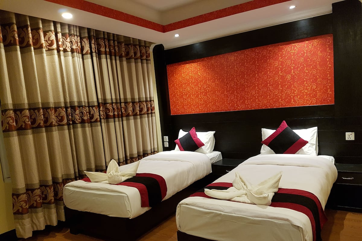 Habitación de hotel con dos camas, un ventanal con cortinas, pared de color rojo con estampado y cabecera negra.