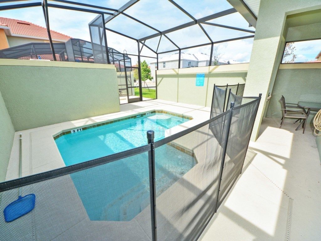 Une piscine couverte, entourée d’une clôture de sécurité, un espace patio avec des chaises et une vue sur le quartier.