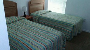 Una habitación con dos camas individuales, cada una con ropa de cama a rayas, una mesita de noche con lámpara y una ventana con persianas.
