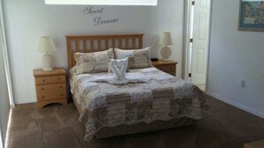 A neatly made bed with a quilt and pillows, two bedside lamps, a wooden nightstand, and a wall with the words "Sweet Dreams" above the bed.