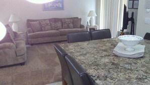 A living room with a sofa, a dining table with chairs, a lamp, and a framed picture on the wall.