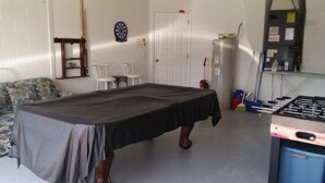 A room with a covered table, a dartboard, a door, a water heater, and a foosball table.