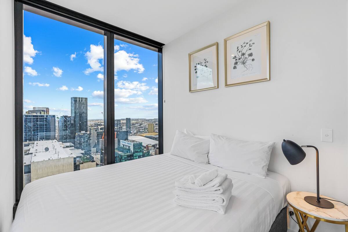 A hotel room with a large bed, a city view, and two framed botanical prints on the wall.