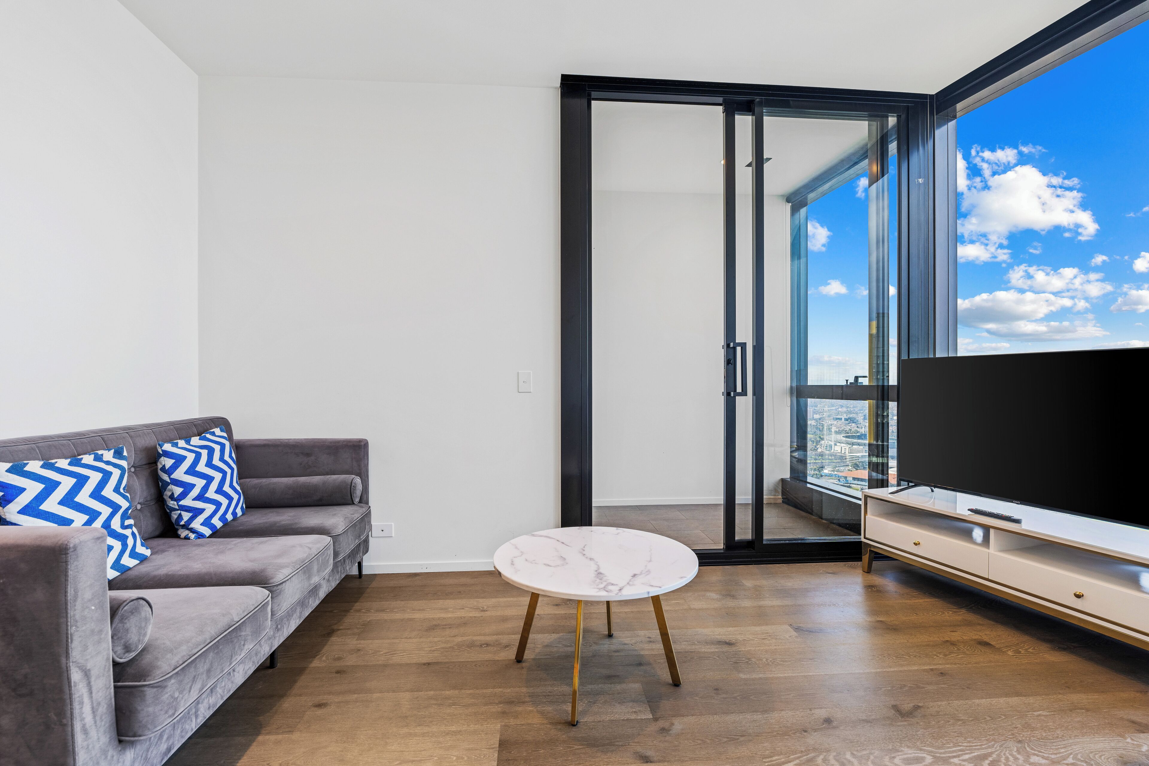 A modern living room with a grey sofa, a white marble coffee table, and a large flat-screen TV.