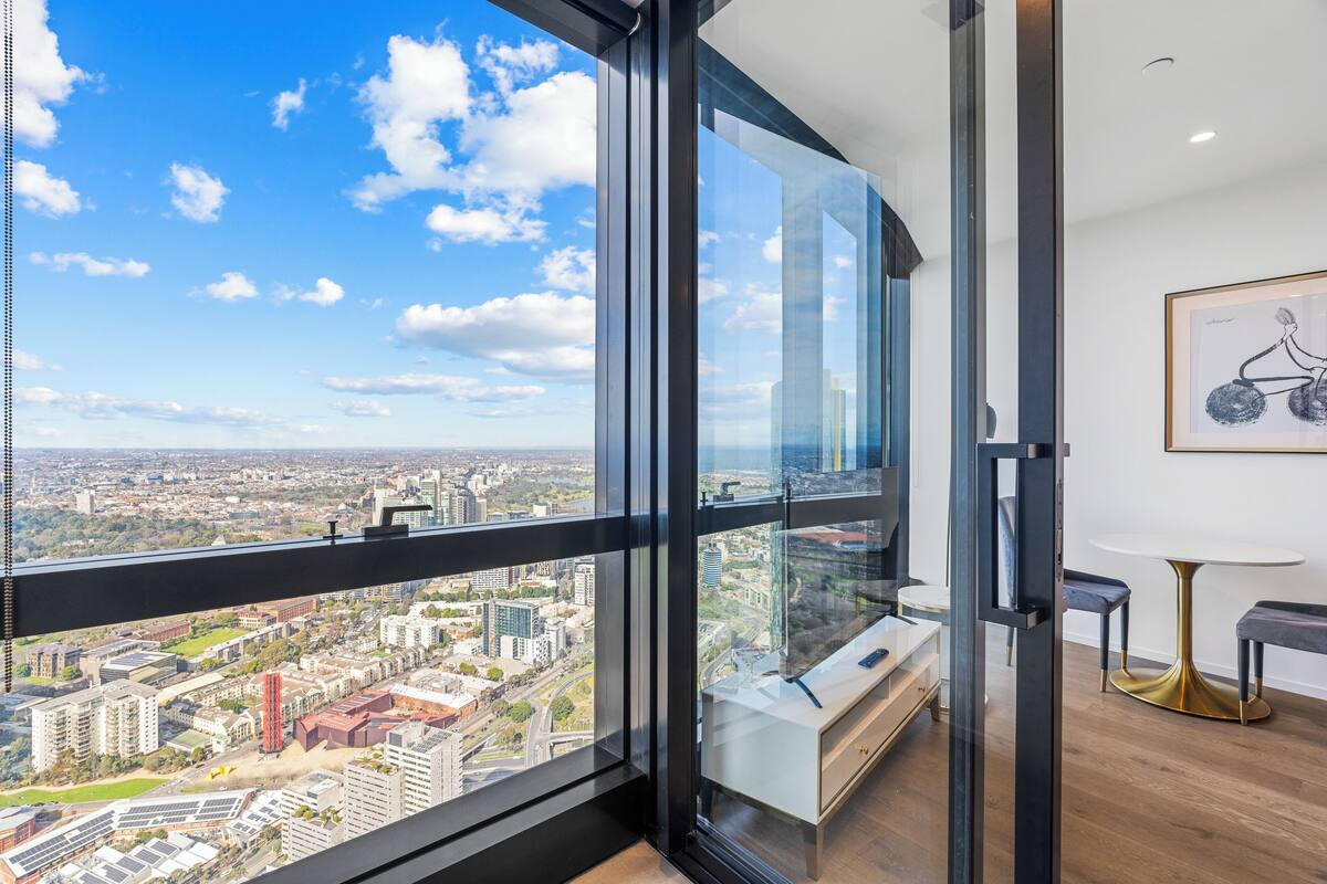 A modern room with a large window offering a city view, a minimalist design, and a small table with a gold base.