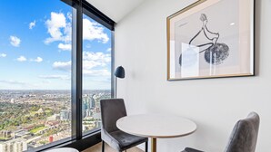 A modern room with a large window offering a city view, a framed artwork, and a small round table.