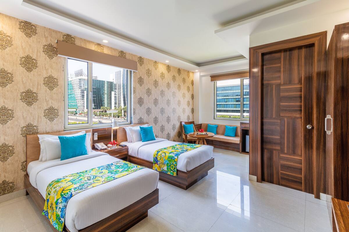 A hotel room with two beds, a sofa, a small table, and a large window.