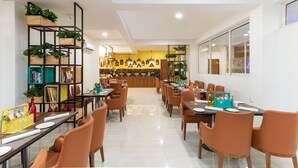 A modern dining area with multiple tables and chairs, a central bar area, and shelves with plants and books. - Inde Hotel Cyber City (Gurugram)