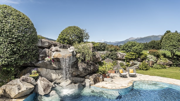 Une piscine agrémentée d’une cascade, entourée de gros rochers et de plantes en pot.