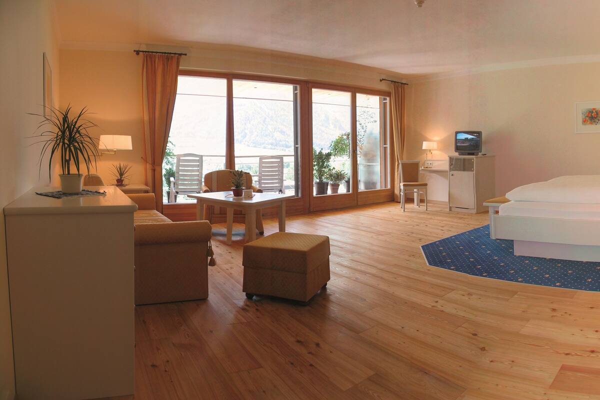 A hotel room with a bed, a desk, a chair, a small table, and a TV.