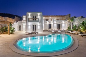 En moderne villa med swimmingpool, udendørs siddepladser og en stenvæg.