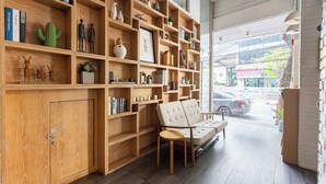 A modern interior with wooden shelving, a cushioned bench, and a view of the street outside. - Simply Sleep Hostel (Bangkok)