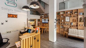 A modern hostel interior with a reception desk, seating area, and a TV. - Simply Sleep Hostel (Bangkok)