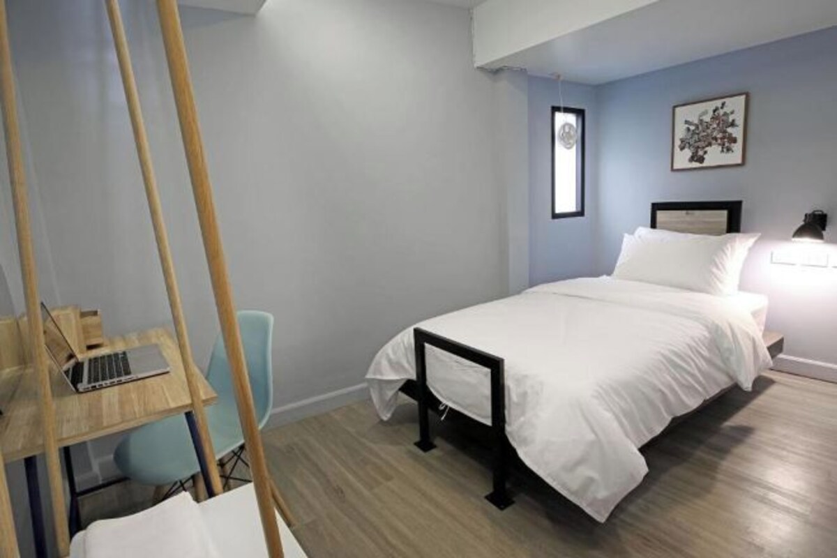 Une chambre à coucher avec un lit, un bureau avec un ordinateur portable, une chaise et une lampe fixée au mur.