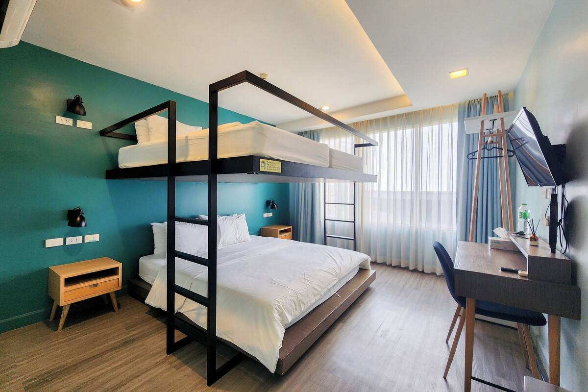 Una cama individual superpuesta con escritorio y silla, una mesita de noche de madera pequeña y un espejo en la pared.