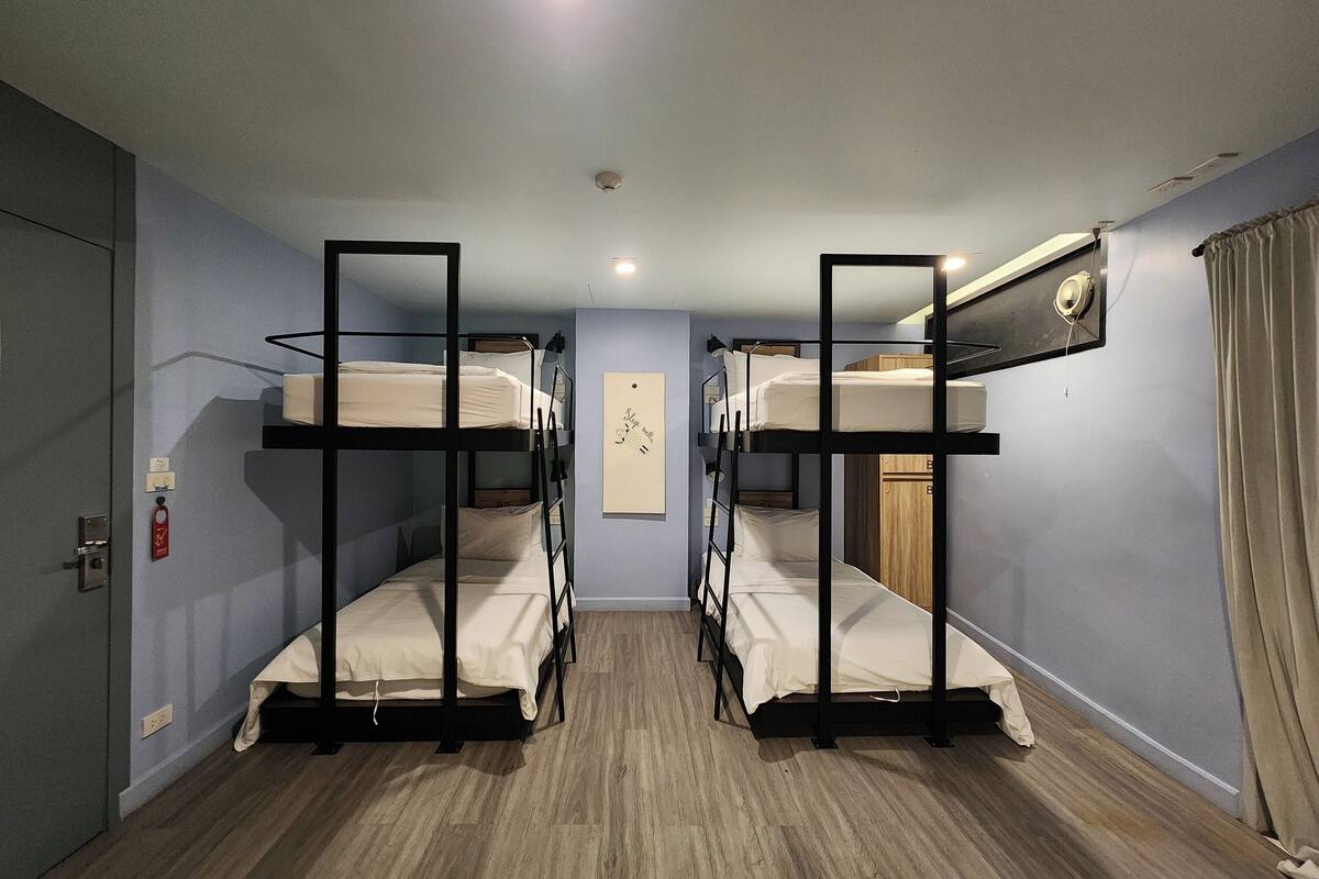 Una habitación con literas, suelo de madera, una puerta y un interruptor de luz.