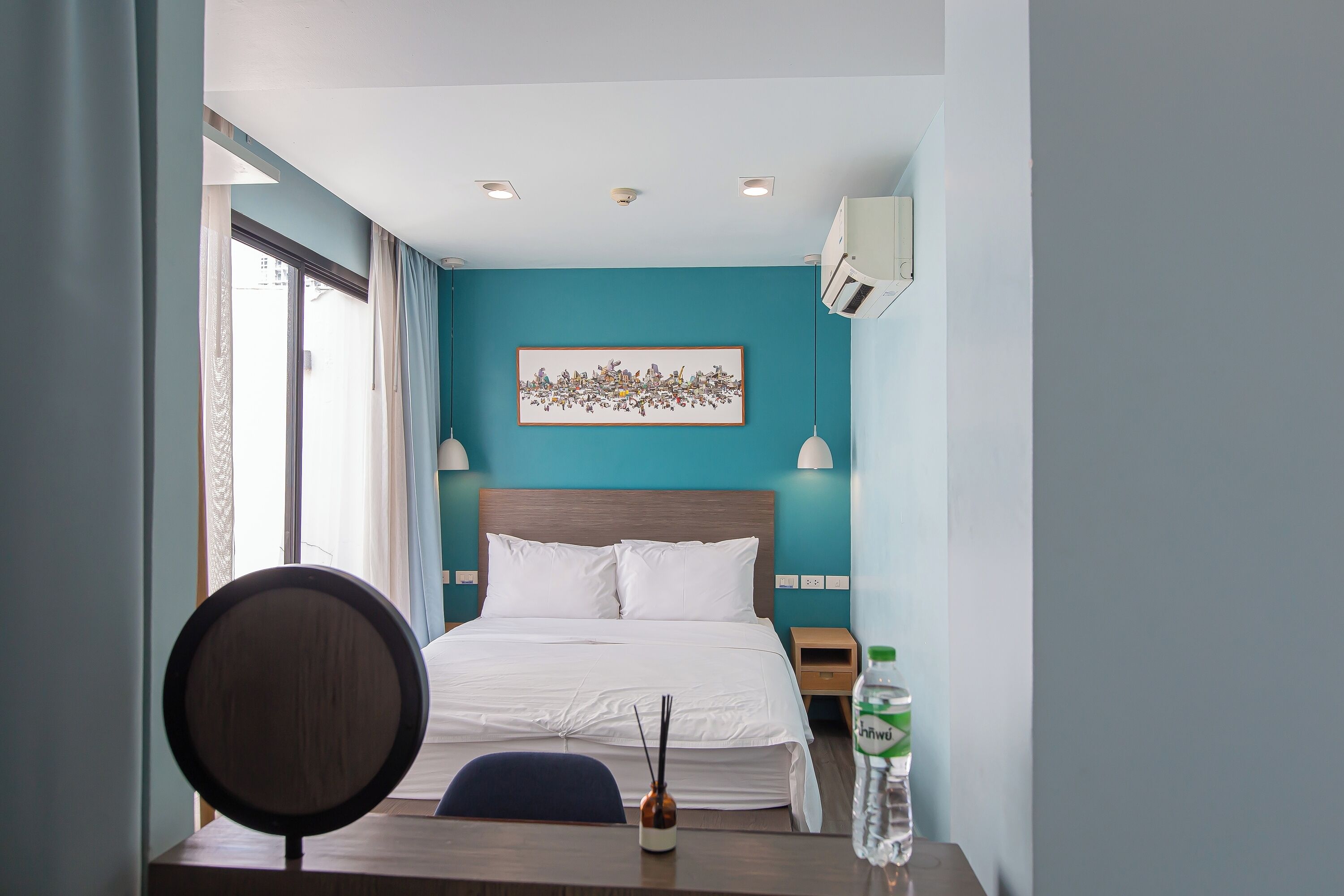 A hotel room with a bed, a desk with a chair, a water bottle, and a framed picture on the wall.