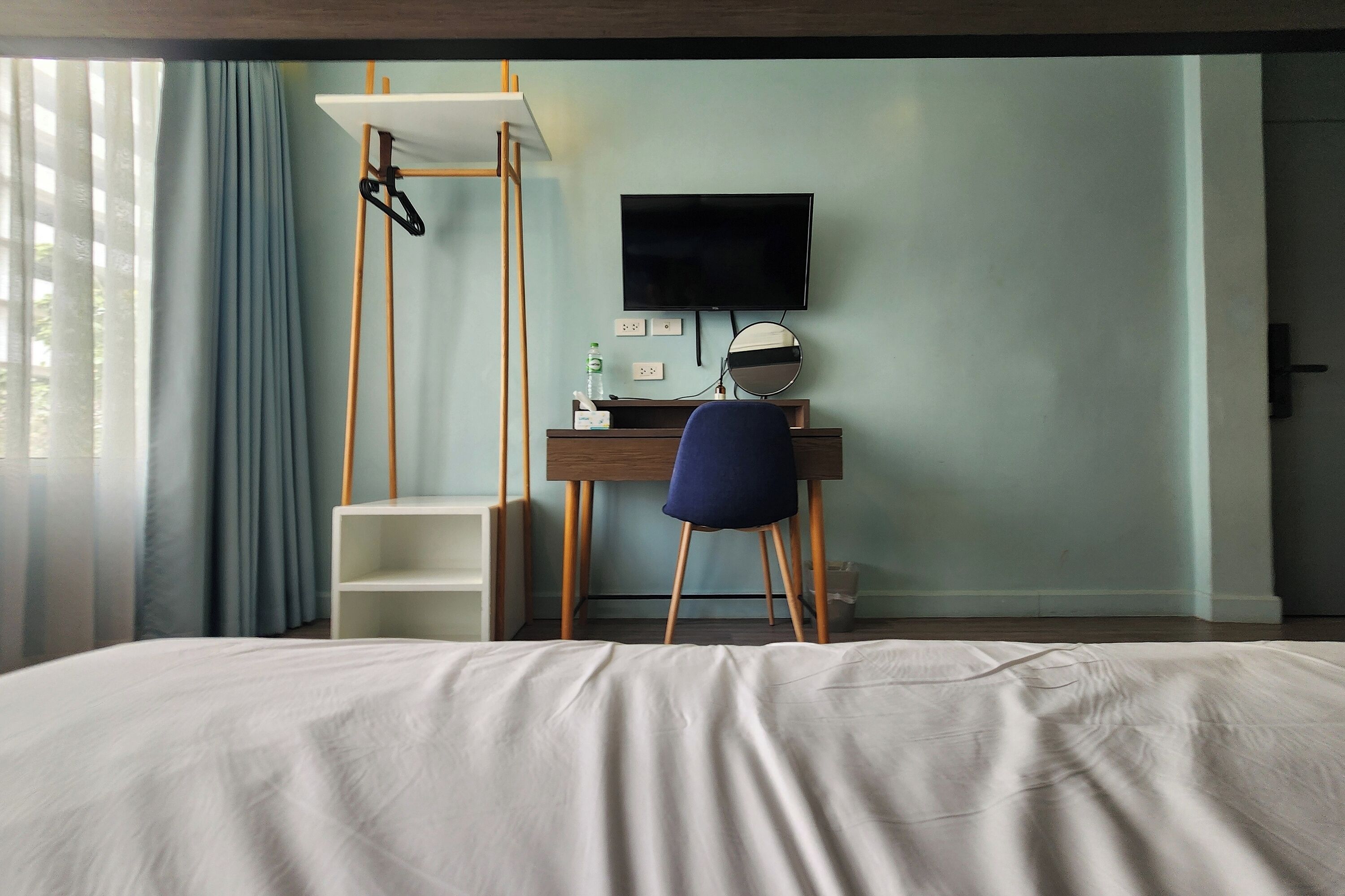 A hotel room with a bed, a desk with a chair, a TV, and a window with curtains.