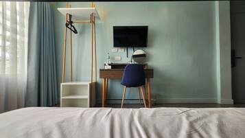 A hotel room with a bed, a desk with a chair, a TV, and a window with curtains.