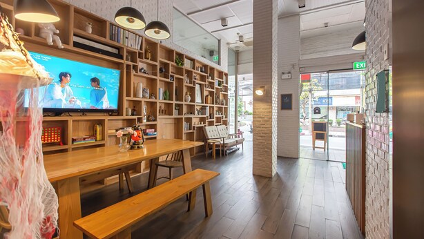 A modern interior with wooden furniture, a television, and shelves with various items. - Simply Sleep Hostel (Bangkok)