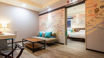 A hotel room with a wooden floor, a sofa with cushions, a small table, and a bed.