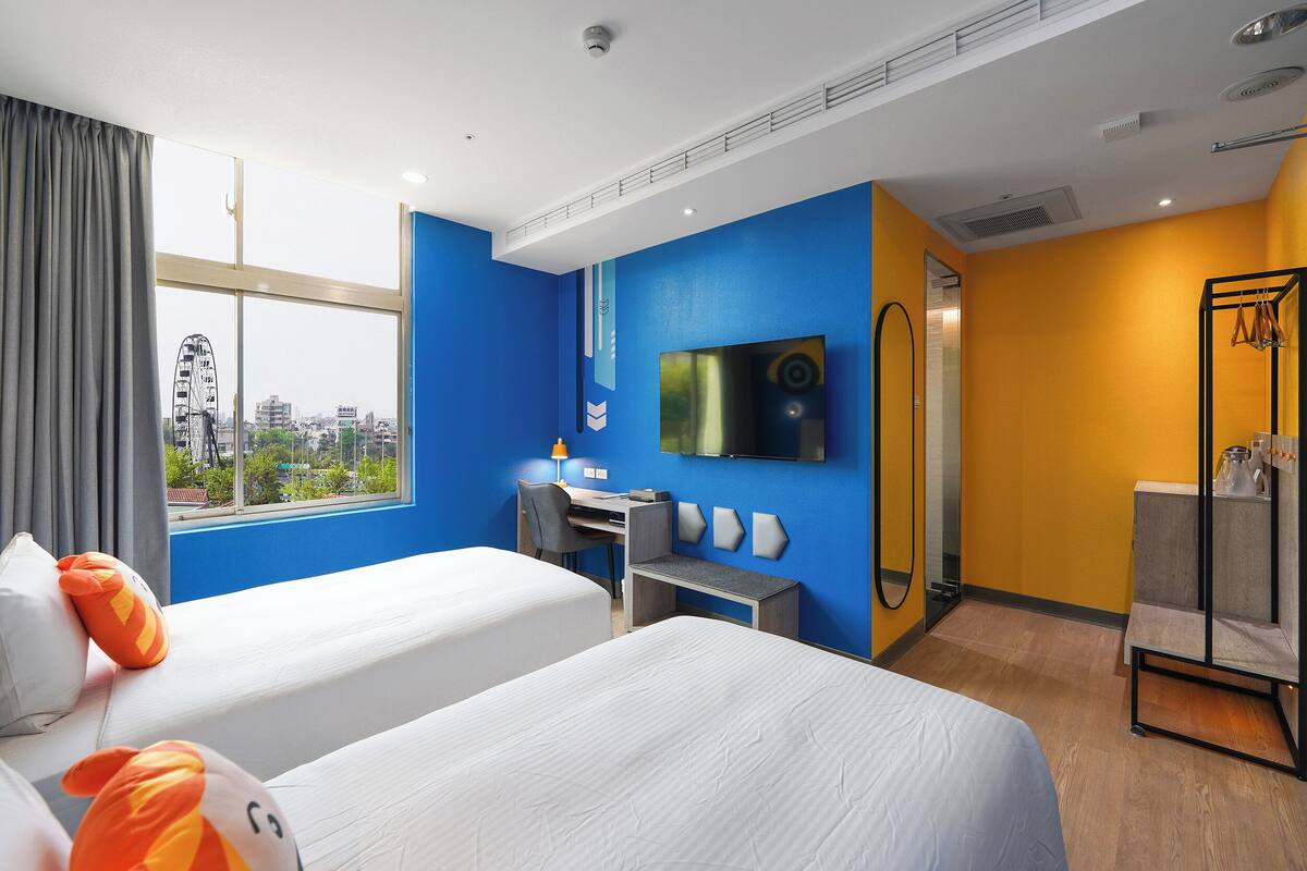 Ett hotellrum med två sängar, ett skrivbord, en TV och utsikt över staden.