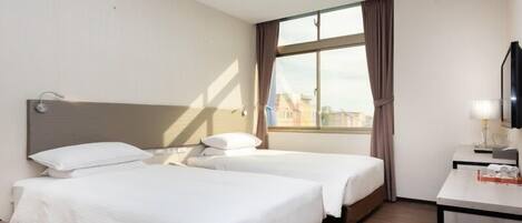 Una habitación de hotel con dos camas, un escritorio, una televisión y una ventana con cortinas.