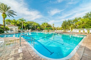 Una piscina rectangular con agua azul cristalina, rodeada por un pavimento de ladrillo y sillones blancos.