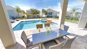 A poolside area with a glass table and wicker chairs, overlooking a swimming pool and a residential neighborhood. - Aco246871 - The Encore Club Resort - 9 Bed 8.5 Baths Villa (Kissimmee)
