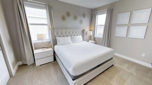 Ein Schlafzimmer mit einem großen Bett, zwei Nachttischen, einem Schminktisch und einem Fenster mit Vorhängen.