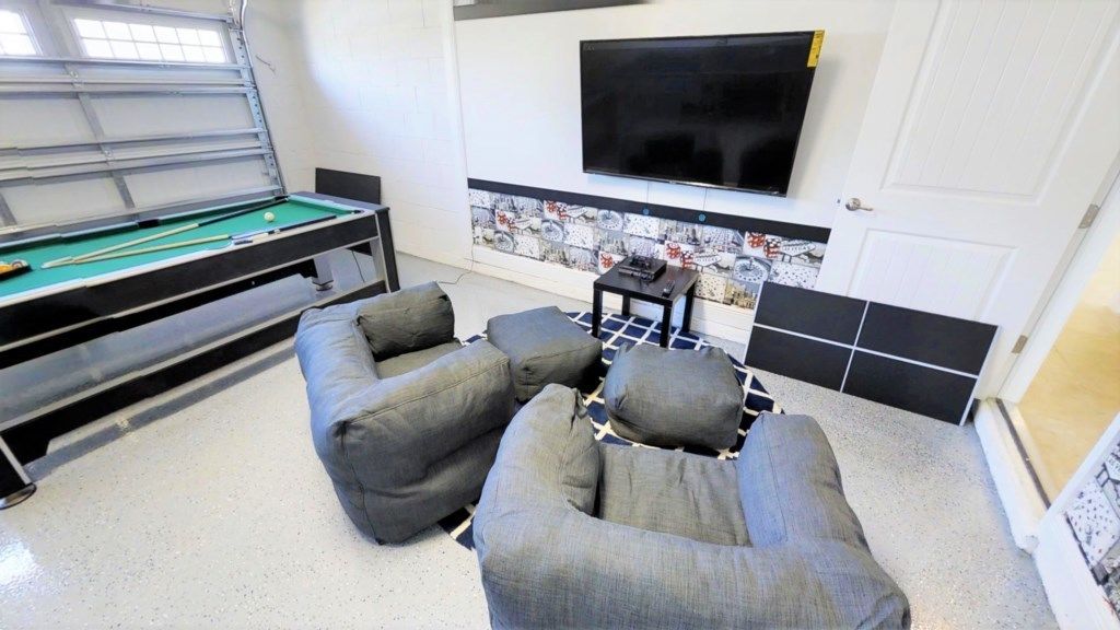 A pool table with cues, a television mounted on the wall, and grey upholstered seating.