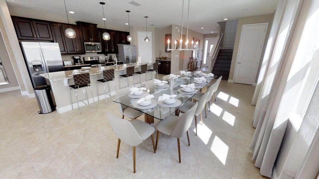 A modern kitchen with dark cabinets, stainless steel appliances, and a dining area with a glass table set for six.