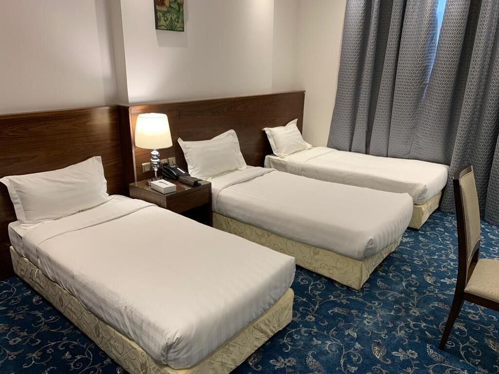 A hotel room with two single beds, a nightstand with a lamp, a telephone, and a chair.