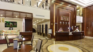 A hotel lobby with a reception desk, seating area, and a food display. - Zaha Al Munawara Hotel (Madinah)
