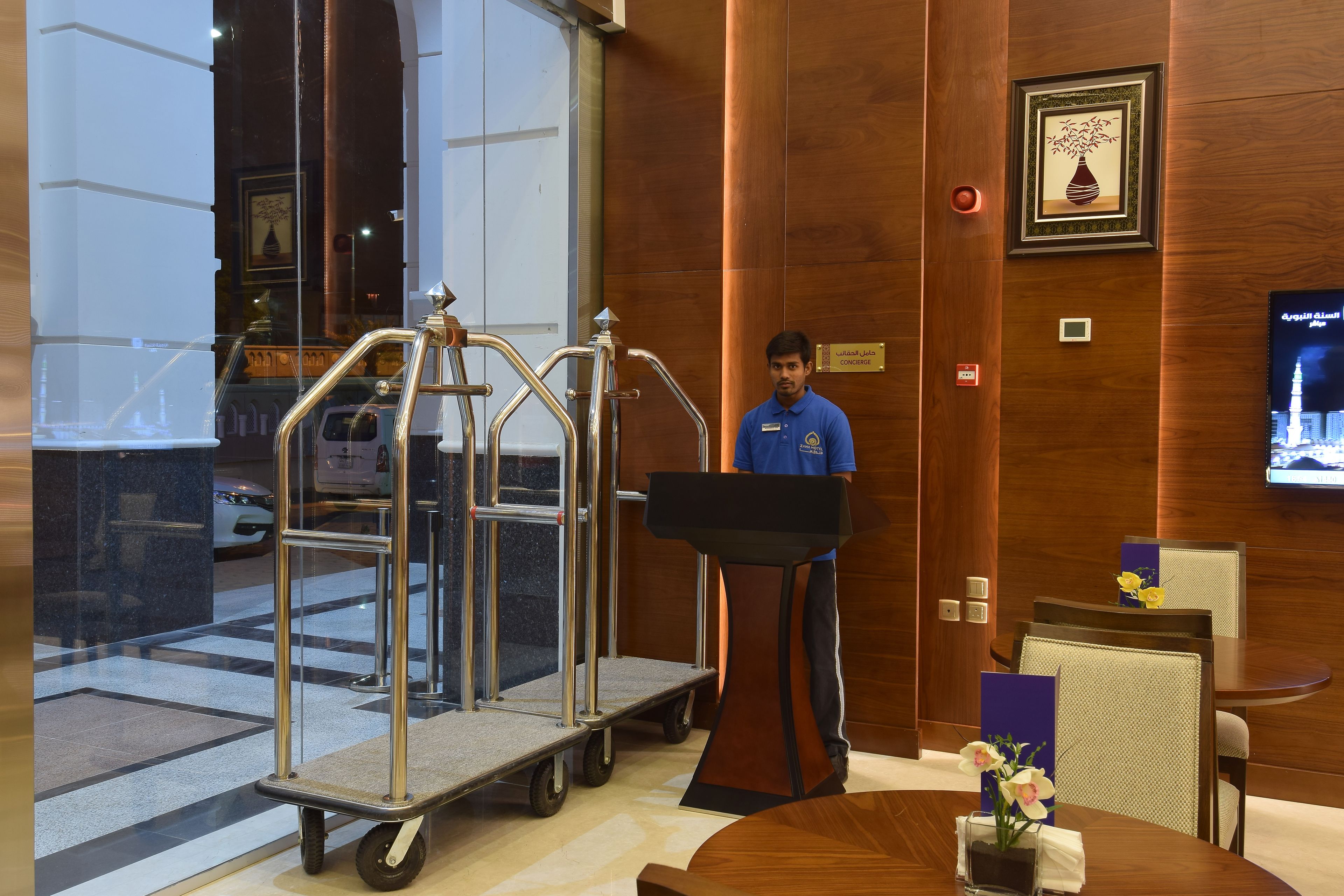 A hotel lobby with a reception desk, a cart, and a television screen.