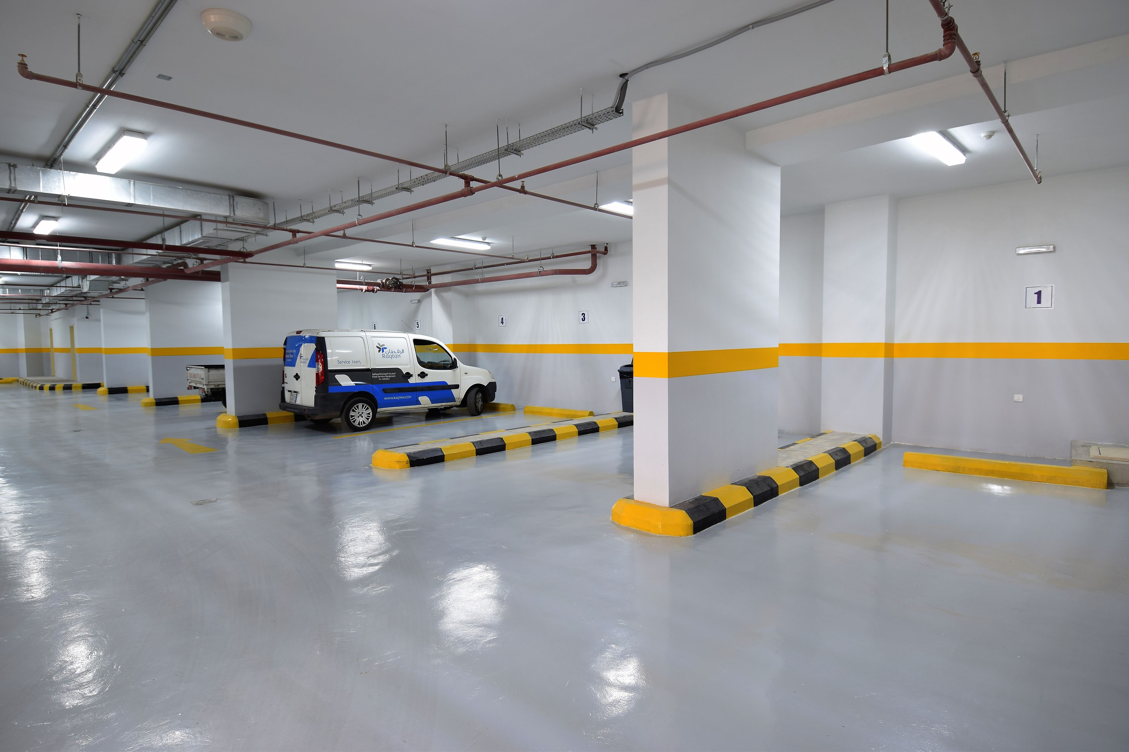 A clean, well-lit parking garage with white walls, yellow and black striped barriers, and a blue and white service vehicle.