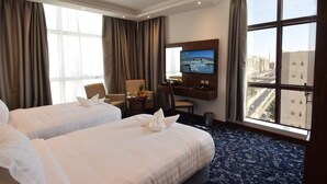 A hotel room with two beds, a desk, a TV, and a large window with a city view. - Zaha Al Munawara Hotel (Madinah)