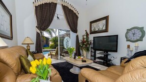 A living room with two leather sofas, a coffee table, a TV, and a clock on the wall. - Ip64290 - Seasons - 4 Bed 3 Baths Villa (Kissimmee)