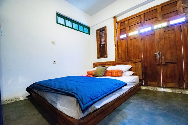 A bedroom with a wooden bed, white walls, a small window, and a wooden wardrobe. - Wave & Chill House (Canggu)