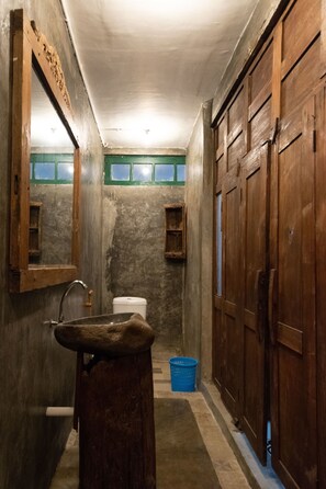 A narrow bathroom with a wooden sink, a toilet, and a wooden wardrobe. - Wave & Chill House (Canggu)