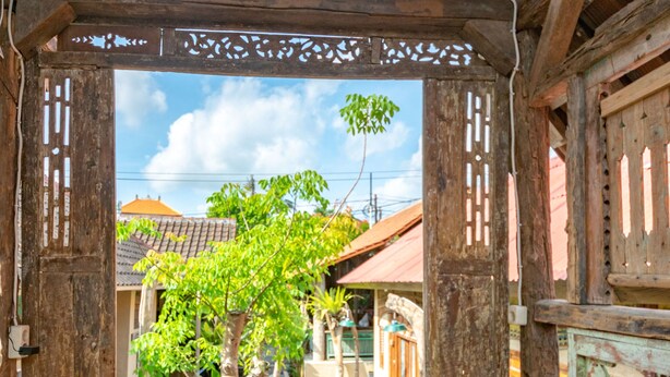 An open wooden structure with a tiled roof, leading to a courtyard with a tree and a pool. - Wave & Chill House (Canggu)