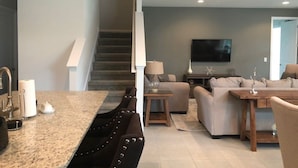 A modern living room with a staircase, a flat-screen TV, a dining area with a marble countertop, and a sofa. - Aco258800 - The Encore Club Resort - 8 Bed 6.5 Baths Villa (Kissimmee)