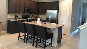 A kitchen with dark wooden cabinets, a stainless steel refrigerator, a microwave, a coffee maker, and a granite countertop island with bar stools. - Aco258800 - The Encore Club Resort - 8 Bed 6.5 Baths Villa (Kissimmee)