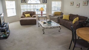 Una sala de estar con alfombra color beige, dos sofás, una mesita de centro y un mueble bajo para televisión con libros.