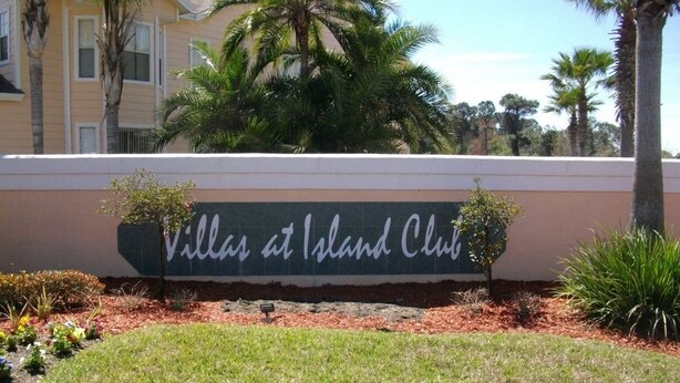 Señal de 'Villas at Island Club', con vista clara del edificio y palmeras circundantes.