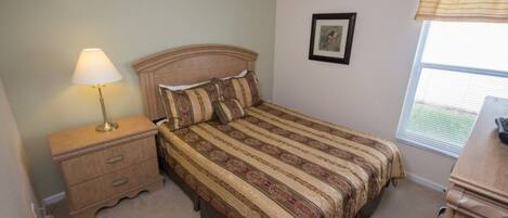 A bedroom with a bed, a nightstand, a lamp, a framed picture on the wall, and a window with blinds.